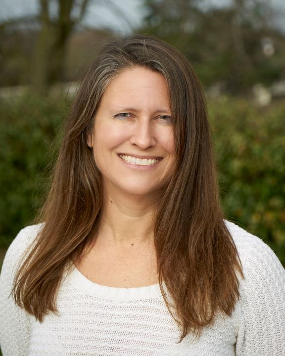 Julie Stephens Senior Biostatistician Outdoor headshot with tall, green bush in the background