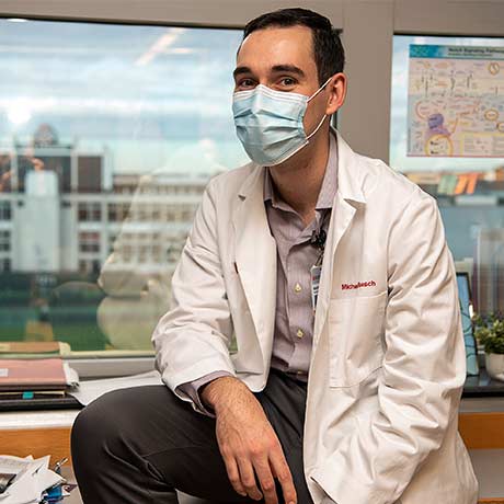 A MSTP student wearing a face mask and lab coat in a research lab