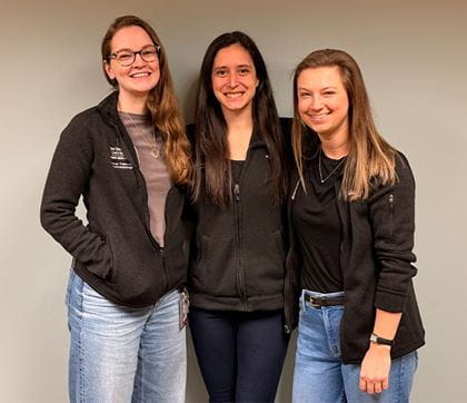 Chief residents dressed in casual wear with arms around each other in front of a wall of plants. 