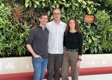 Chief residents dressed in casual wear with arms around each other in front of a wall of plants. 