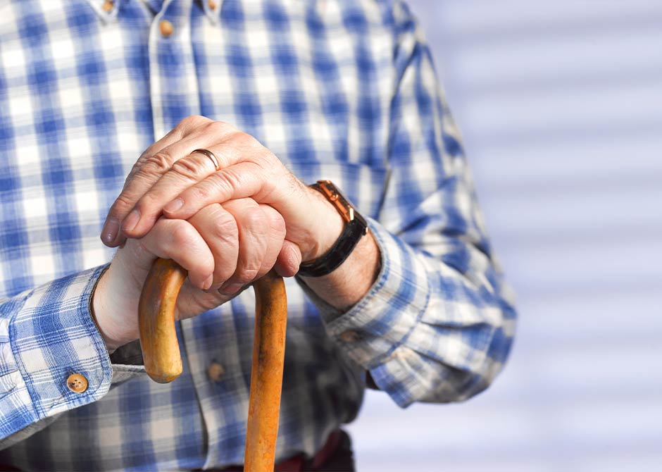 Close up of a pensioner resting his hands on a walking stick