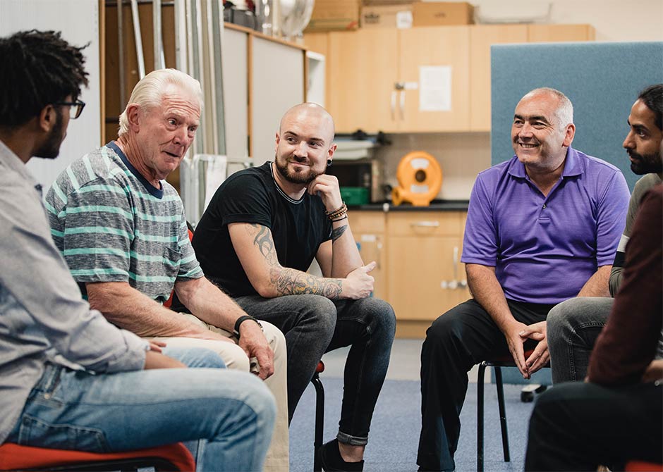 Diverse group of men are talking and laughing together in a mental health support group.