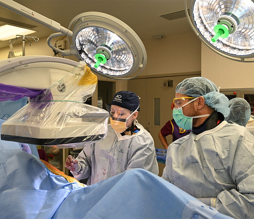 Surgeons in a brightly lit operating room, wearing protective gear and focused intently on a procedure.