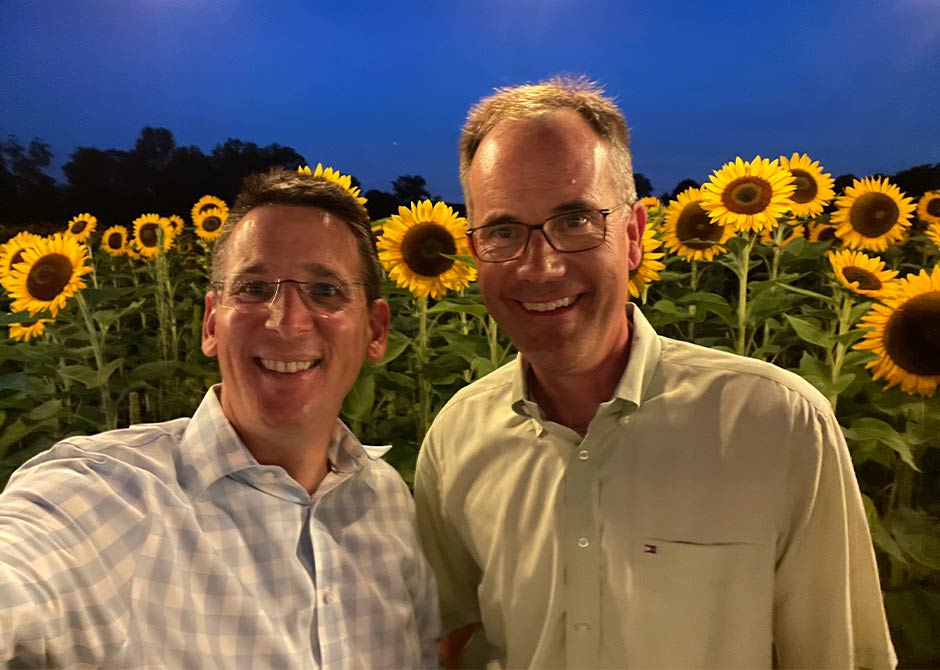 two men in front of a field of sunflowers