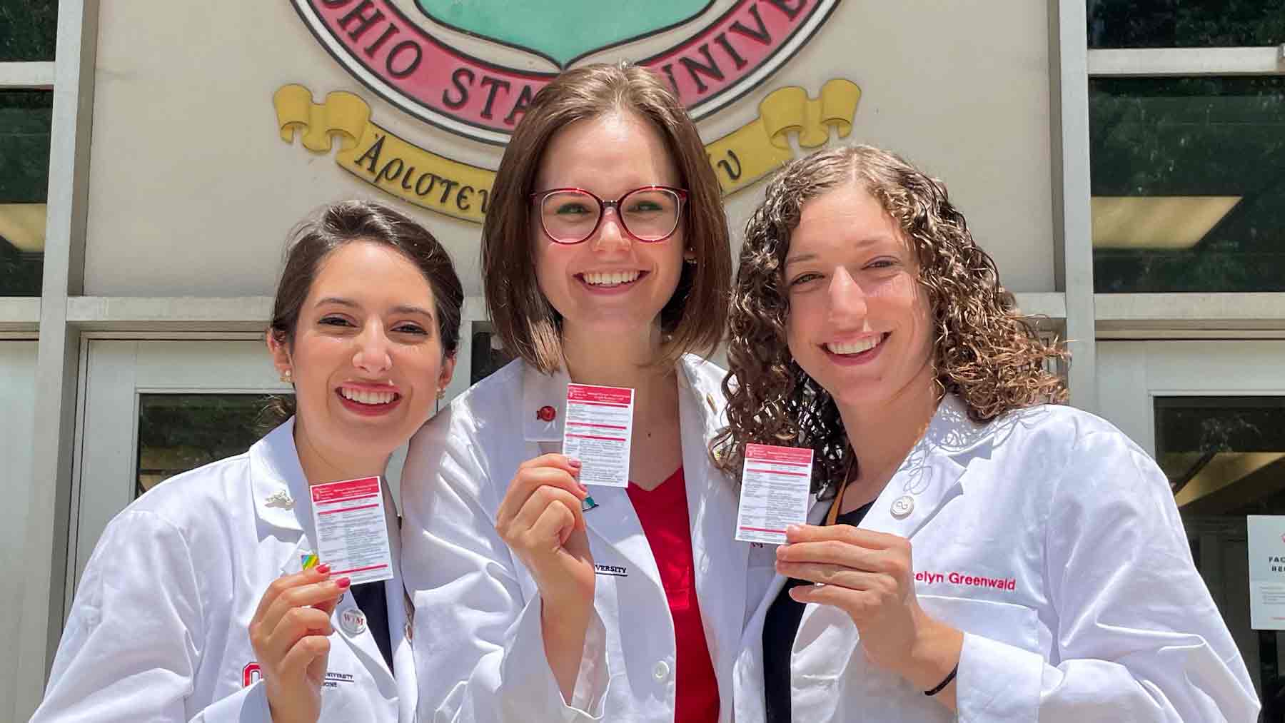 Three women in white coats holding resource cards