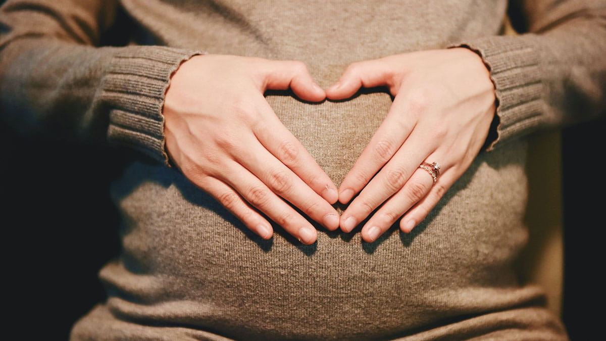 Hands shaped like a heart over a pregnant belly