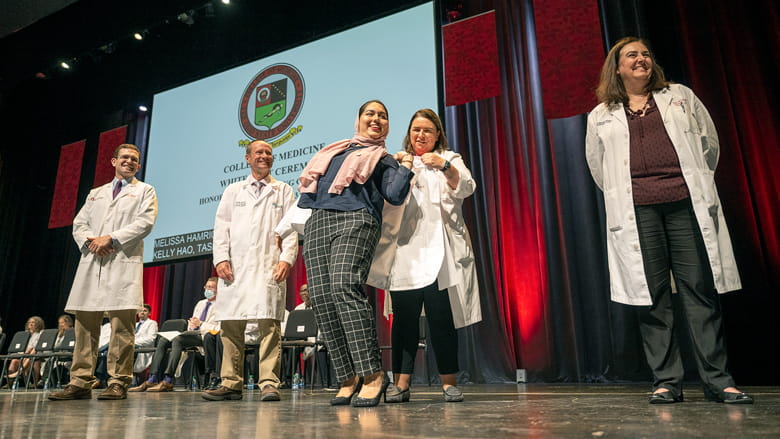 Student putting on her white coat on stage