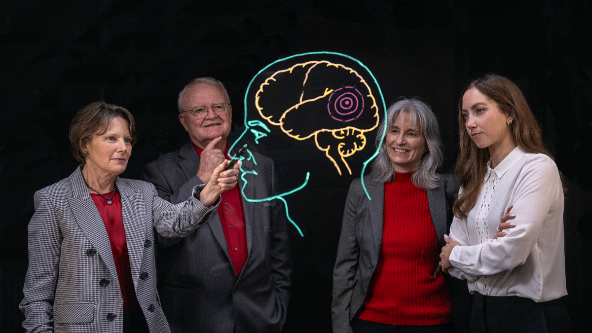 Image of four people gathered around drawing a picture of a human head with a brain.