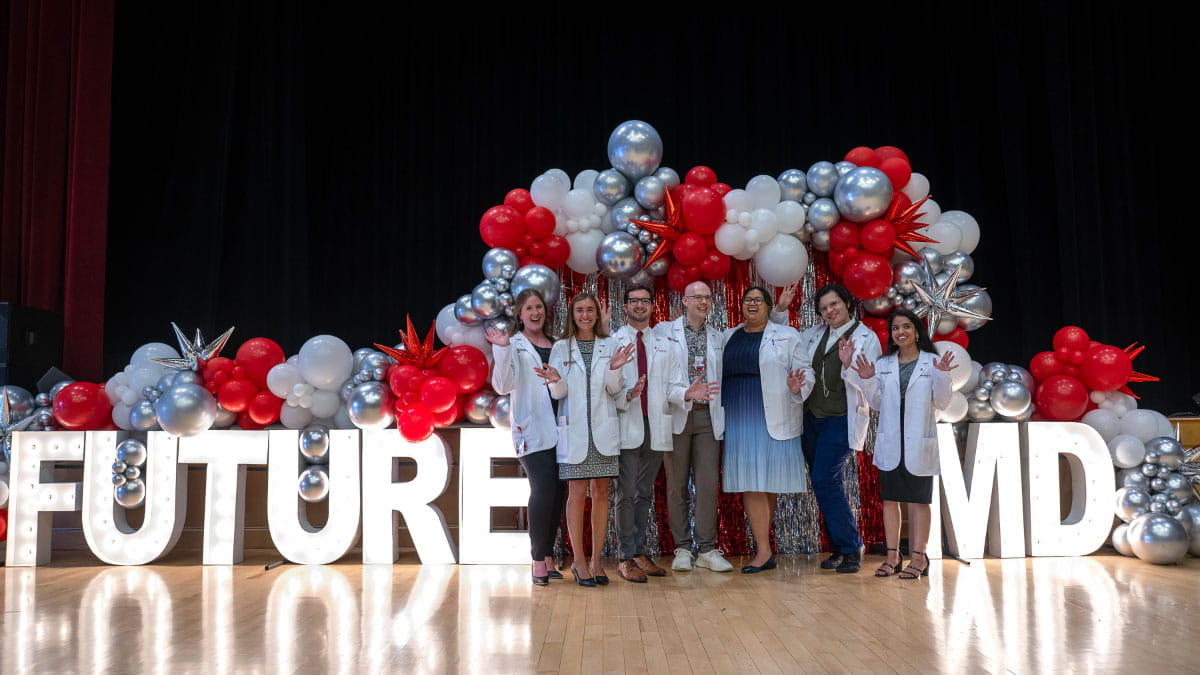 Image of students standing in front of a balloon arch in their white coats.