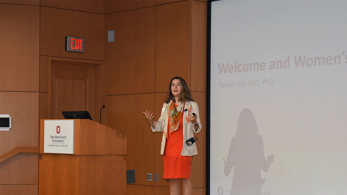 Image of Tamar Gur speaking at a podium