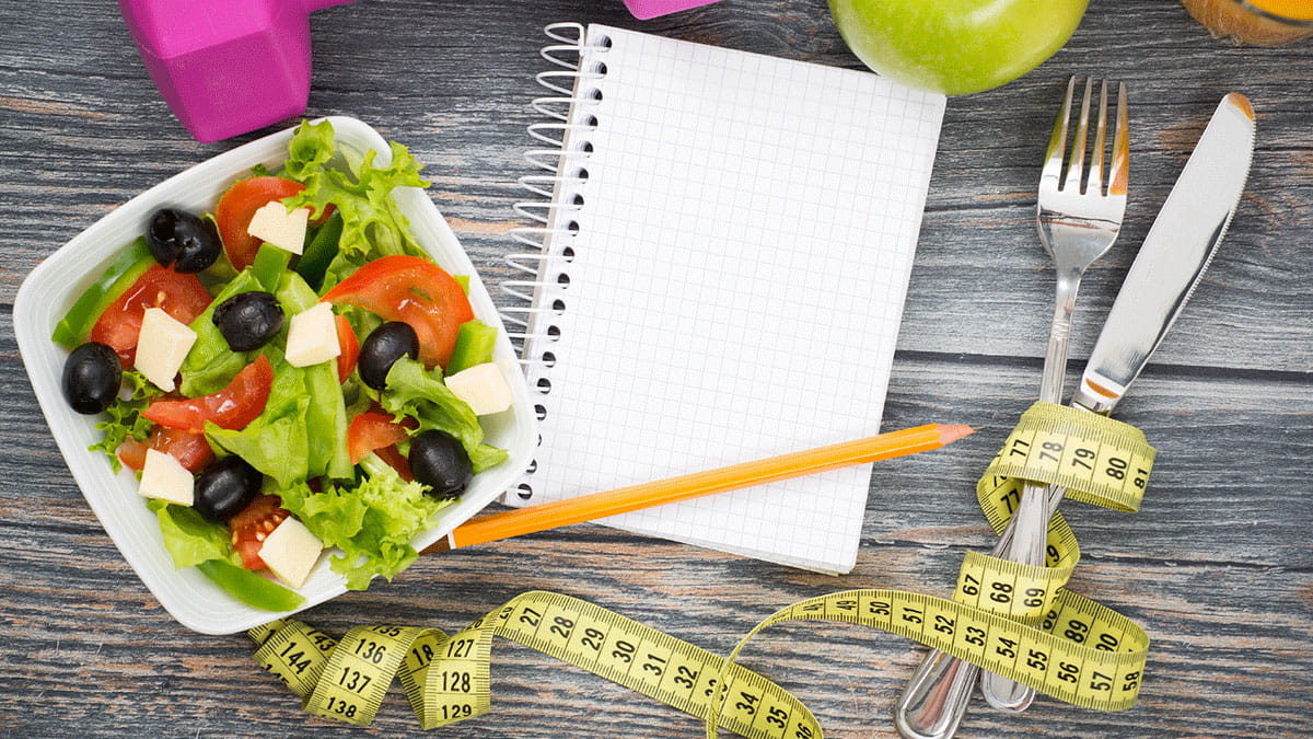 Image of a salad, a notebook, and a measuring tape.
