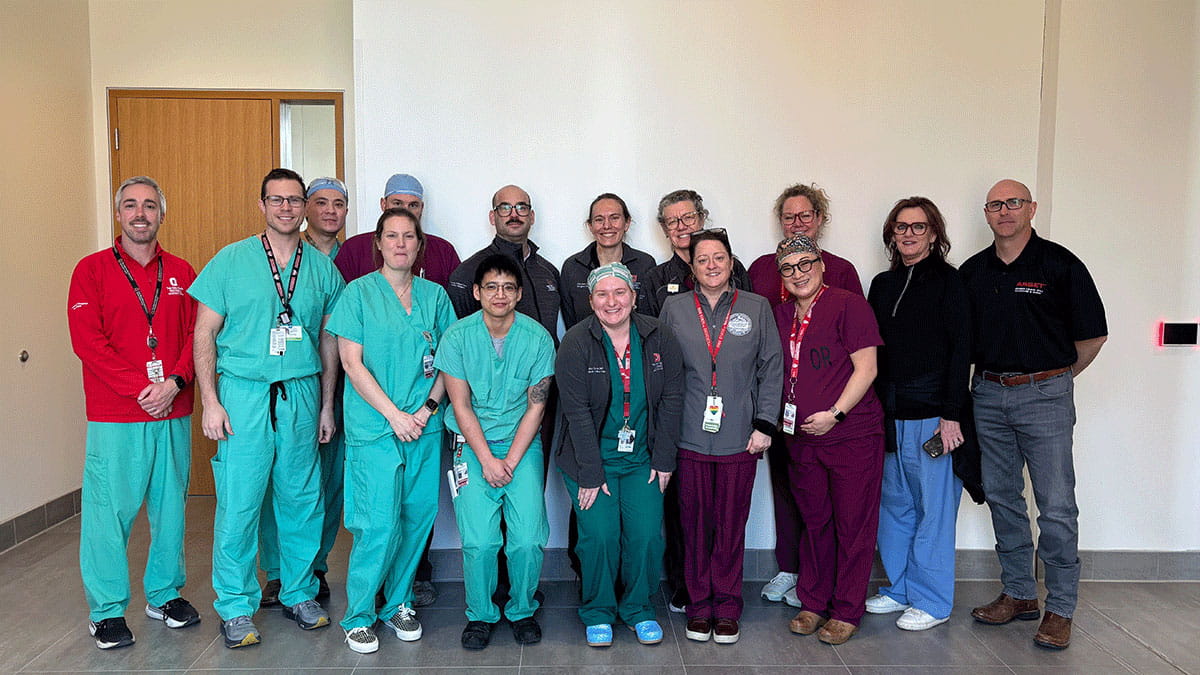 A diverse group of 14 medical professionals pose together, smiling. 