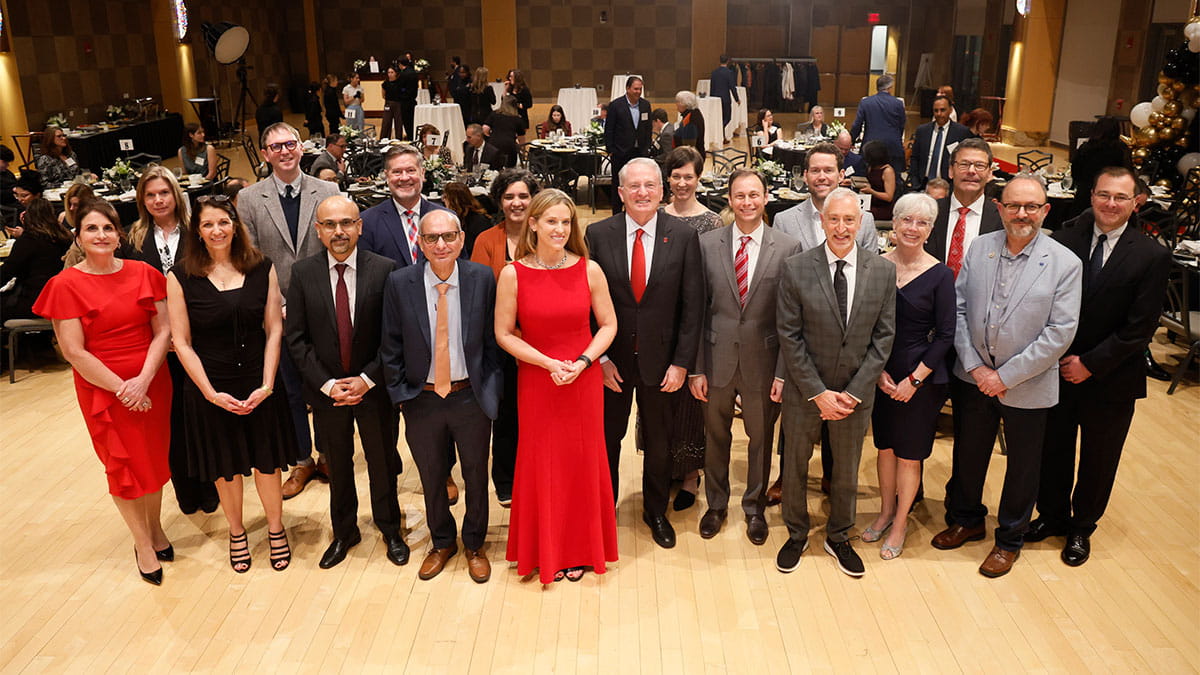 A diverse group of 19 people, dressed formally, pose in a warmly lit banquet hall.