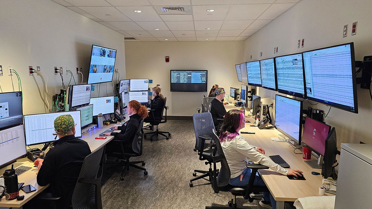 A room with eight people seated at desks, each monitoring multiple computer screens displaying data.