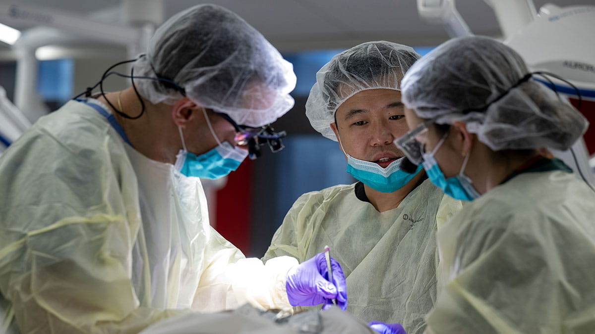 Three doctors performing a surgical operation, focused on a patient, dressed in surgical attire including gowns and masks.