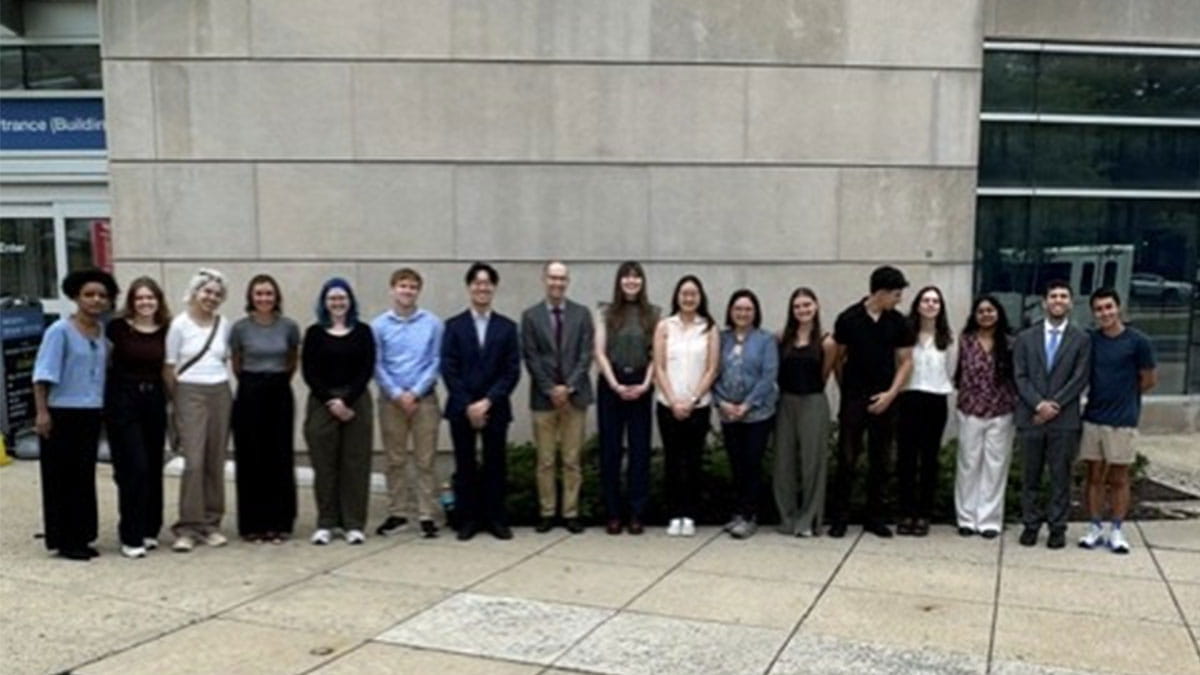 Group of 17 people posing outside a modern building.