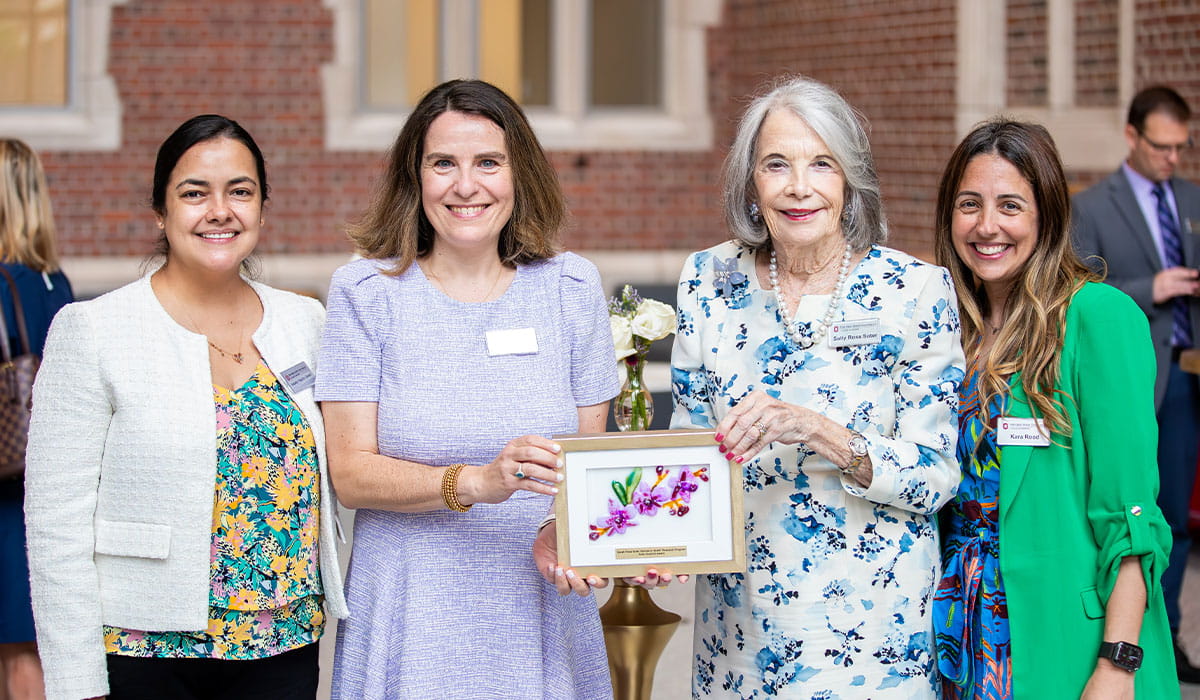 Four smiling women stand in an indoor setting, one holding a framed award.