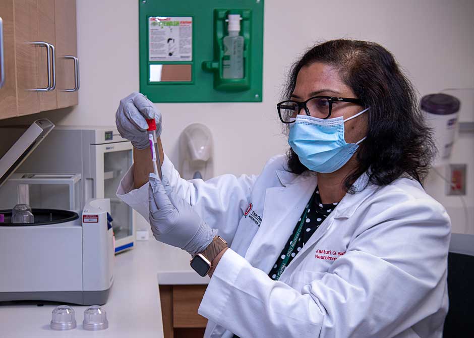 Neuroimmunology researcher inspecting vial in lab wearing face mask